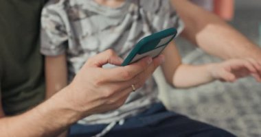 Bir baba, oğluna mobil uygulamadan çamaşır makinesini nasıl kullanacağını gösteriyor. Programı çalıştırıyor, kapıyı kapatıyor ve telefonu ile başlıyor. Ev işlerinde modernlik.