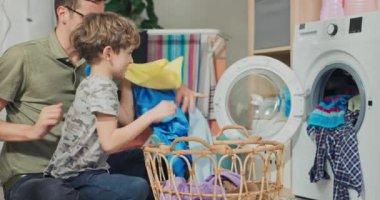 Çocuk babasının kirli çamaşırlarını çamaşır makinesine koymasına yardım ediyor, hasır sepetten bir şeyler çıkarıyorlar, çocuk ona yardım ettiği için gururla gülümsüyor ve beşlik çakıyor..