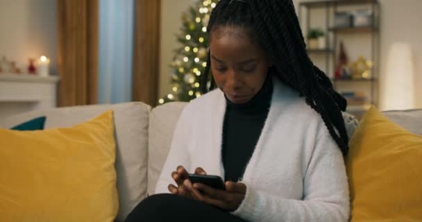 Attractive Girl African Appearance Sits Couch Holding Phone Choosing Ordering — Vídeos de Stock