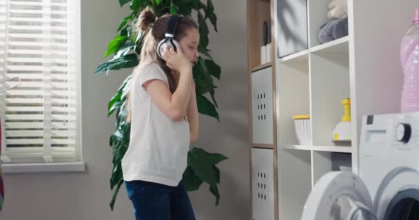 Усміхнена Дівчина Навушниках Прослуховування Музики Входить Пральню Приймає Капсулу Білизни — стокове відео