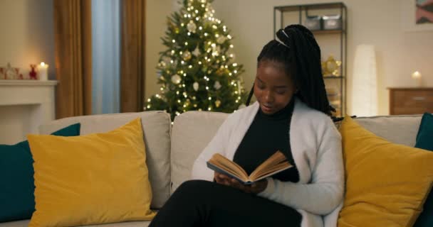 Una Chica Aspecto Africano Sienta Sofá Sosteniendo Libro Cubierta Azul — Vídeo de stock