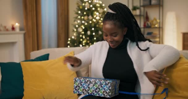 African Looking Girl Pigtails Sits Sofa Living Room Holds Gift — Stockvideo