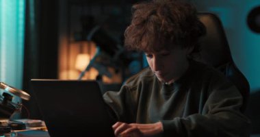 Ödev yapan genç çocuk bilgisayarla odada tek başına oturuyor. Ergen laptop 'da video izliyor ve internette geziniyor..