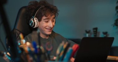 Kıvırcık saçlı genç bir çocuk uzaktan öğrenmeyle mutludur. Bir öğrenci kablosuz kulaklıklı bir bilgisayarın önünde oturuyor ve bir öğretmenin dersini dinliyor. Dersler internet üzerinden yapılıyor..