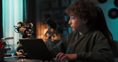 Ergen karanlıkta oturuyor ve bir robotu dizüstü bilgisayara programlıyor, yeni özellikler ekliyor, beşlik çakıyor, robot teknolojisine ilgi gösteriyor..