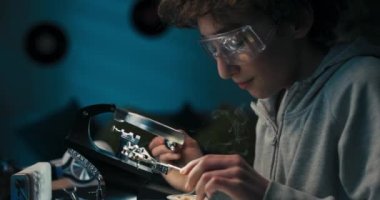 Child spends free time at desk learning to solder, cares about safety, boy has safety goggles, repairs cables, electronics, smoke rises.