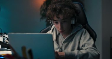 A child designs a building for tech class, does homework, draws with a pencil in a notebook, looks at a computer screen with graphics on. A boys room with a desk, vinyl records on the wall.