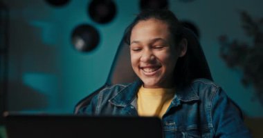 Portrait of a young pretty teenage girl who studies sitting at a desk with a laptop at home, the girl talks to her friend via webcam laughs jokes.