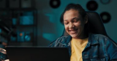 Evde dizüstü bilgisayarla masa başında oturan genç ve güzel bir kızın portresi. Kız arkadaşıyla kamera şakalarıyla konuşuyor..