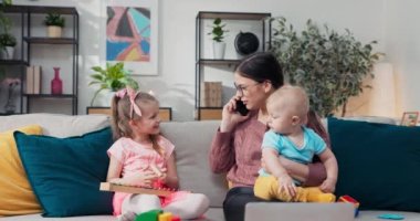 Young, beautiful woman talking on cell phone. Mother playing with children while working. A girl gossiping with husband via smartphone while keeping an eye on son and daughter.