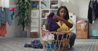 Genç bir anne çamaşır odasında yerde otururken ev işi yapar. Kadın çamaşırları katlar, giysileri ayırır, banyoyu temizler..