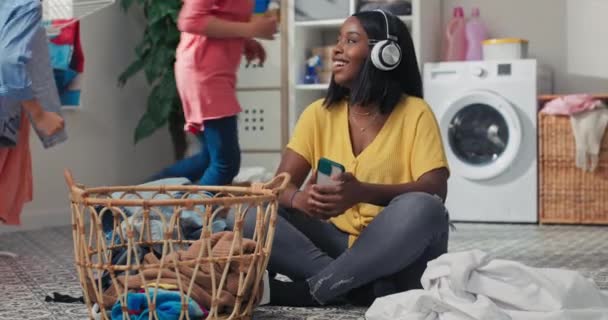 Smiling Woman Headphones Sits Bathroom Floor Laundry Room Sorts Colorful — 图库视频影像