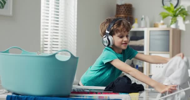Boy Wearing Wireless Headphones Stands Stool Laundry Room Fold Out — Vídeos de Stock