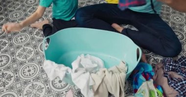 Overhead shot of a bowl of clothes being sorted by a dad with his son with the correct colors for the washing machine throwing things in.