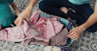 Overhead shot of a bowl of clothes being sorted by a dad with his son by their respective colors for wash in a washing machine.