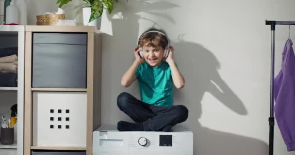 Small Child Sits Washing Machine Wireless Headphones Listening Music Nodding — Stock Video