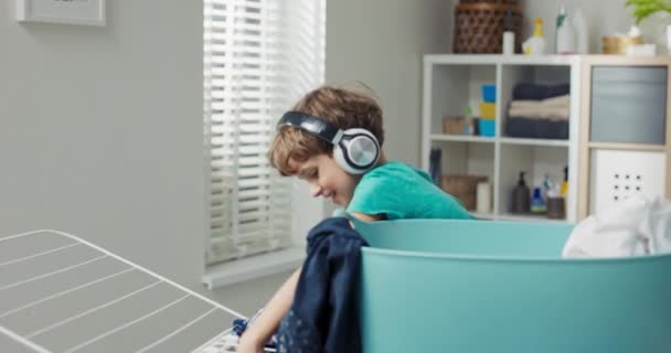 Boy Curly Hair Wearing Wireless Headphones Stands Clothes Dryer Child — Stock Video