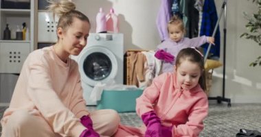 Shared laundry room bathroom cleaning. Mom and two daughters high-five with rubber-gloved hands. The girls play while sweeping mopping the floor.
