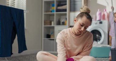 Cleaning concept at home. A woman sits on the bathroom floor in the laundry room scrubbing the floor with a liquid cloth wearing rubber pink gloves. Smiling girl likes tidiness.