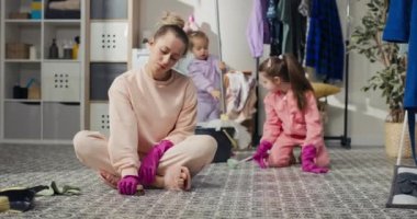 Cleaning concept at home. A woman sits on the bathroom floor in the laundry room scrubbing the floor with a liquid cloth wearing rubber pink gloves. Smiling girl likes tidiness.