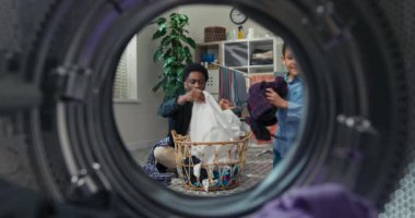 Portrait of a young man with his brother folding laundry, sorting clothes into the washing machine, morning housework, cleaning. View from inside the drum.