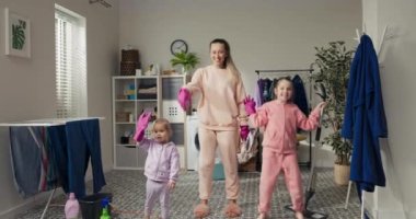 Hafta sonu temizlik konsepti. Anne ve iki kızı çamaşır odasını, banyoyu temizliyor. Kadınlar ve küçük kızlar yerleri süpürürler, yerleri süpürürler, dans ederler, müzik dinlerler, birlikte eğlenirler..