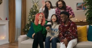 En iyi beş arkadaş oturma odasında kanepede oturup görüntülü konuşma yapıyorlar. Arkadaşlar el sallar, gülümser ve sarılırlar. Arkalarında süsler ve Noel ağacı var. Erkekler ve kızlar iletişim kurar ve eğlenirler..