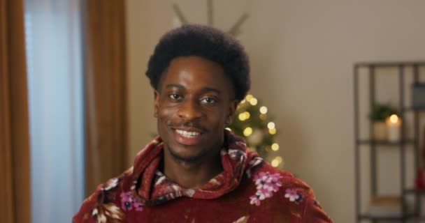 Young Guy African Appearance Sincerely Smiling Christmas Tree Flickering Room — Vídeo de stock