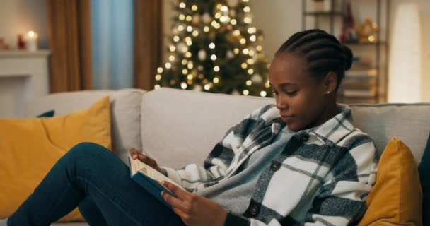 Atrakcyjna Dziewczyna Afrykańskim Wyglądzie Siedzi Kanapie Trzyma Książkę Niebieską Okładką — Wideo stockowe