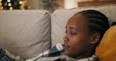 Üzgün bir Afrikalı kız ekose gömlek giyiyor, oturma odasında kanepede uzanıyor ve film izliyor. Duygulandı, dudağını ısırdı ve filmin kahramanları için endişelendi..