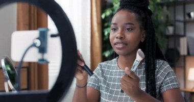 At kuyruğu örgülü koyu tenli bir kadın doğru makyaj fırçalarını nasıl seçeceğine dair kısa talimat videoları kaydetti. Kız sosyal medyada güzellik içeriği yaratıyor..