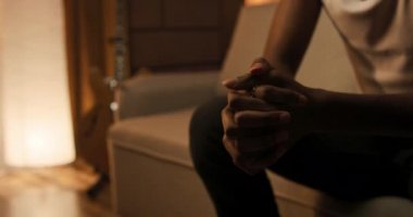 Close up portrait of a man of African American descent sitting on a couch worried sad looking ahead with tears in his eyes reliving the loss of a loved one, room lit with golden sunlight