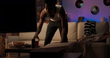 Afro adam bir kutu pizzayla odaya girer oturma odasındaki koltukta oturur, en sevdiği TV programını tek başına izler, aksiyon hakkında heyecanlanır, cips yer..