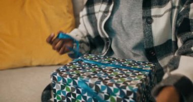 Kareli gömlek giymiş Afrikalı bir kız kanepeye oturur ve hediyesini açar. Mavi kurdeleyi çözüyor, kutuyu açıyor ve gördüklerine üzülüyor. O, hoşnutsuzluk içinde kutuyu bir kenara attı..