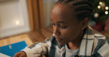 Afrika görünümlü çekici bir kız oturma odasında masada oturuyor. Kız kareli gömlek giyiyor, elinde kağıtlar tutuyor ve konferans raporlarını okuyor. Metne odaklanıyor..