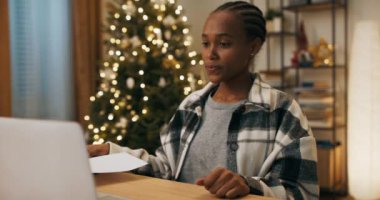 Afrikalı görünümlü bir öğrenci masada oturup görüntülü konuşma yapıyor. Elinde kağıt parçası olan bir kız. Dersi dikkatle dinler ve meslektaşlarıyla tartışır. Odada bir Noel ağacı sallanıyor..