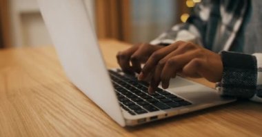 Dizüstü bilgisayarda yazı yazan Afrikalı bir kızın yakın çekimi. Laptop ahşap masada duruyor. Arkasında bir Noel ağacı sallanıyor. Kız ekose gömlek giyiyor..