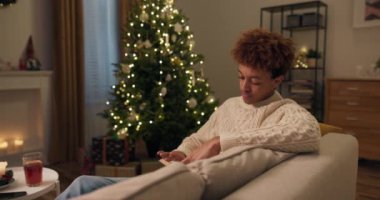 Yakışıklı, güler yüzlü bir adamın portresi kanepede oturmuş kitap okuyor, rahat, şen şakrak atmosfer, Noel ağacının cazibesi..