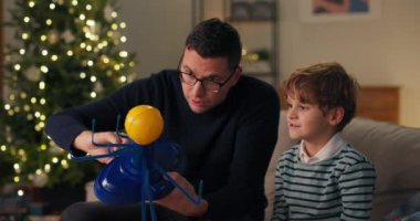 Neşeli çocuk amcasıyla kanepede oturuyor. İnsanın elinde tuttuğu güneş sisteminin modeline bakacaklar. Çocuğa gezegeni gezdiriyor. Odada bir Noel ağacı sallanıyor..