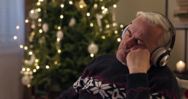 Zimowy Wieczór Starszy Mężczyzna Siedzi Przy Choince Słucha Relaksującej Muzyki — Wideo stockowe