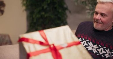 Orta yaşlı bir adamın oğluyla hediyelerini değiş tokuş etmesi. Adam gülümser ve sevinir. Hediye aldı ve kırmızı kurdeleyi çözdü. Sürpriz yapmayı bekleyen ve kalın kazak giyen bir adam..