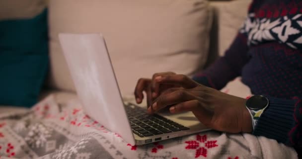 在手提电脑键盘上打字的看上去像非洲人的人的密切合作 这个男孩穿着保暖的假日毛衣 手里拿着手表 耳边放着球 他专心打字 — 图库视频影像