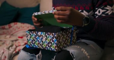 Noel hediyelerini açan Afrikalı görünümlü adamın ellerini yakın plan çek. Oğlan kalın bir süveter ve Noel Baba şapkası giyer, kız kardeşiyle görüntülü sohbet eder, gülümser ve sürpriz için teşekkürler..