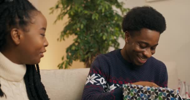 笑着的非洲学生交换圣诞礼物 一个有魅力的男人打开盒子 对他朋友送给他的新耳机感到满意 朋友们拥抱和微笑 — 图库视频影像
