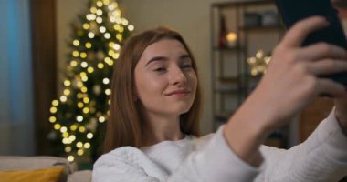 Kış akşamı. Uzun saçlı bir öğrenci oturma odasındaki kanepede oturur ve selfie çeker. Kız elinde telefonla poz veriyor. O beyaz kazak giyiyor. Arkasında titreyen bir Noel ağacı.
