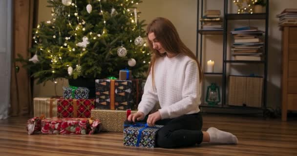 クリスマスツリーの下に積み上げ床の上にクリスマスギフトボックスを詰め女性はゲストを待っています Diyクリスマスや新年の包装コンセプト — ストック動画