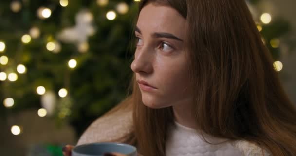 お茶のカップを保持クリスマスツリーに座って悲しい不満の少女のクローズアップ 彼女は長い爪を黒いニスで覆われている 少女はボーイフレンドと別れた ほとんど泣き — ストック動画
