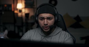 Siyah şapkalı adamın online oyun oynadığı yakın plan fotoğraf. Adamın kafasında kulaklık var ve oyuncularla konuşuyor. Çocuk final maçında oynuyor ve kaybediyor. Kulaklıklarını çıkarıyor, yenilgiden korkuyor..