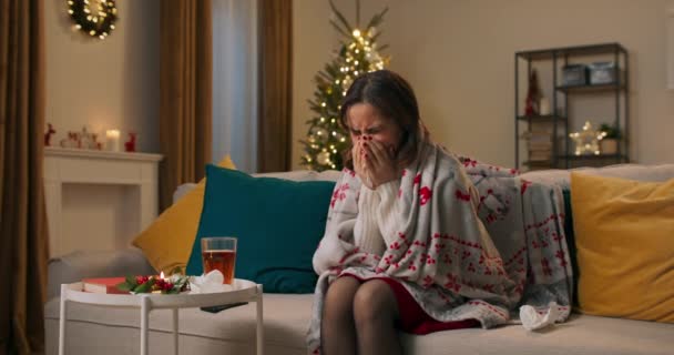 病気の女の子ホールド紙ハンカチ打撃鼻スニーズにハンカチ持ってインフルエンザ熱冷座ってホームの下に毛布の上にザ カウチ上のクリスマス 洞病ウイルス — ストック動画