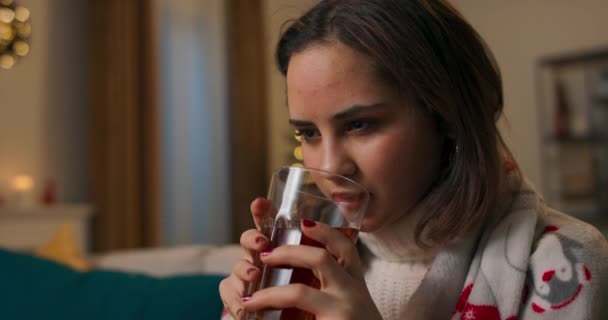 悲しい若い女の子はクリスマスを一人で過ごしている 女性はレモンバームハーブティーを飲む家族や友人がこの冬の夜に彼女を残している彼女の怒りを和らげるために — ストック動画